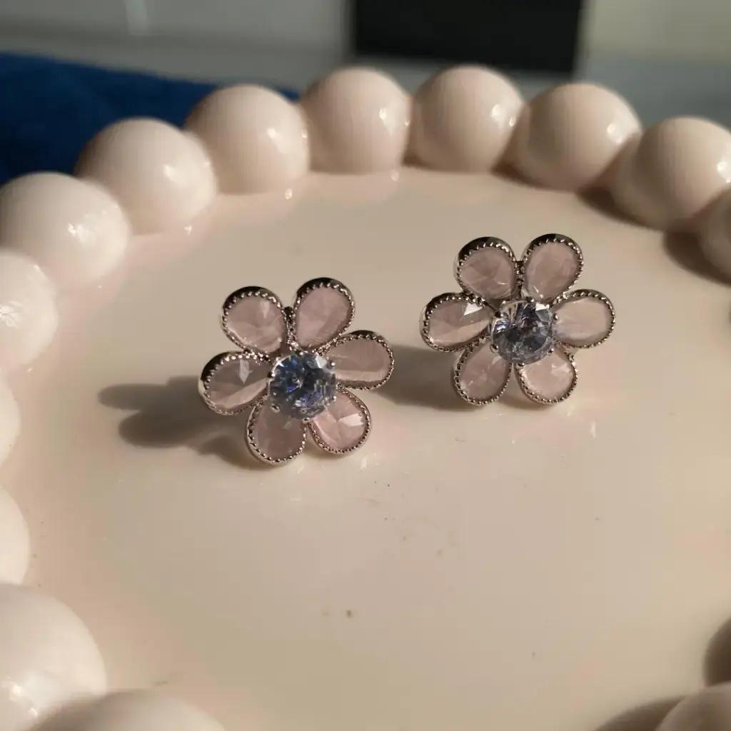 Five soft pink petals inside a milled silver-tone frame with a clear stone at the centre