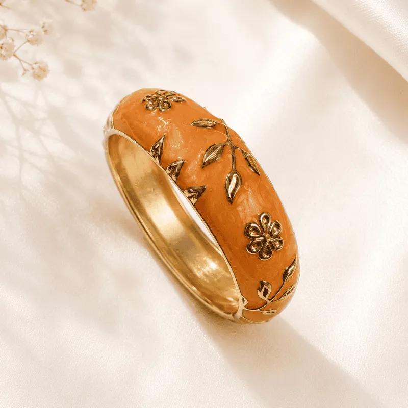 Solid gold-tone kada with raised flowers and trailing leaves in warm orange enamel