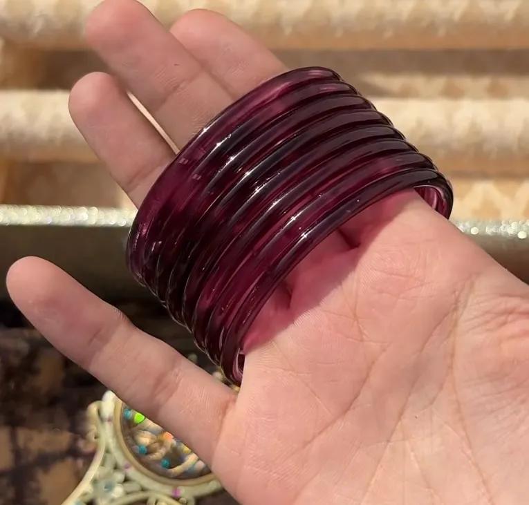 Stack of translucent deep maroon jelly glass bangles held in a hand against a woven gold clutch