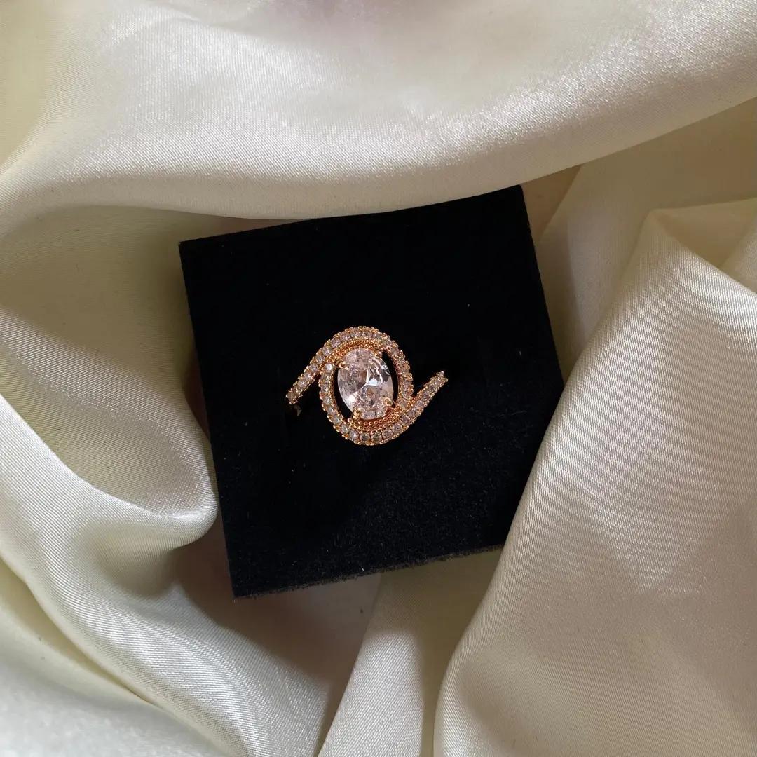 Large oval cubic zirconia ring with a swirling pavé halo in rose gold plating, displayed on a black jewellery box