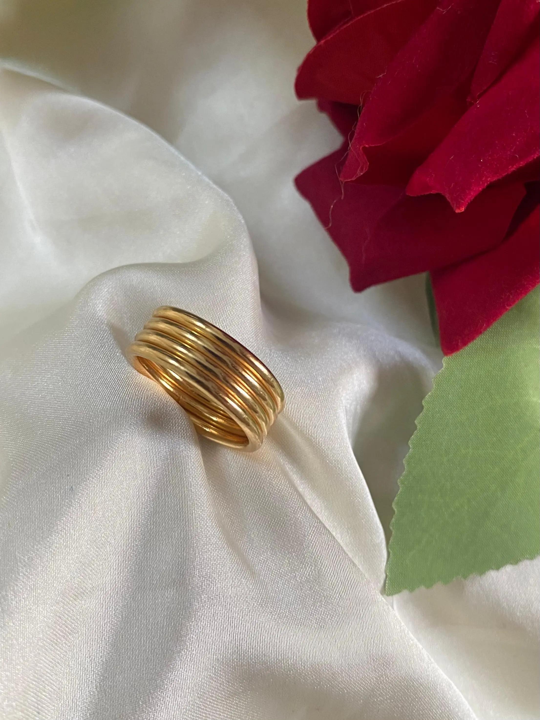 Wide golden ring formed of five fused polished coils resting on white satin beside a red rose