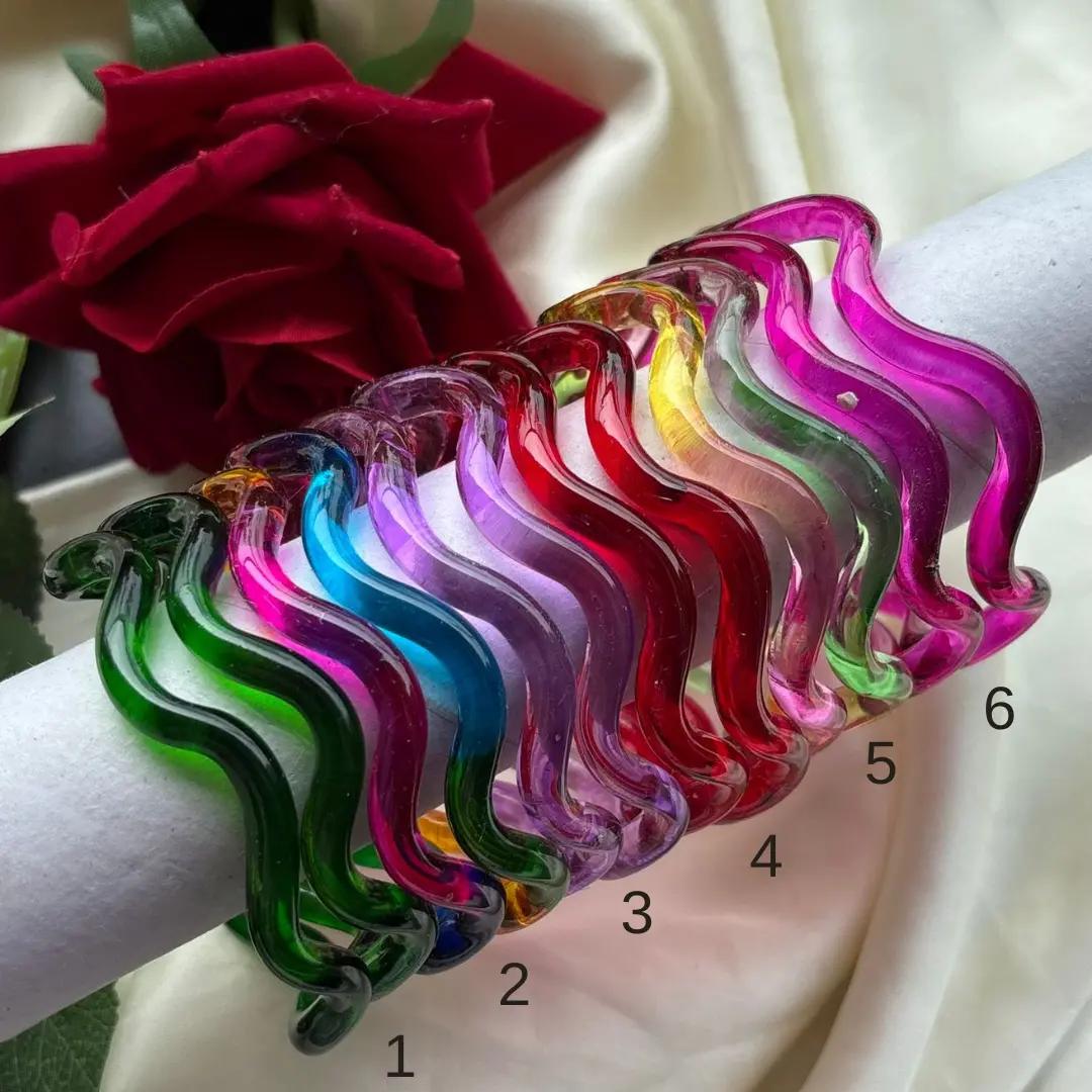 Six wavy glass kangan in green, blue, purple, red, yellow and magenta stacked on a white roll, numbered one to six
