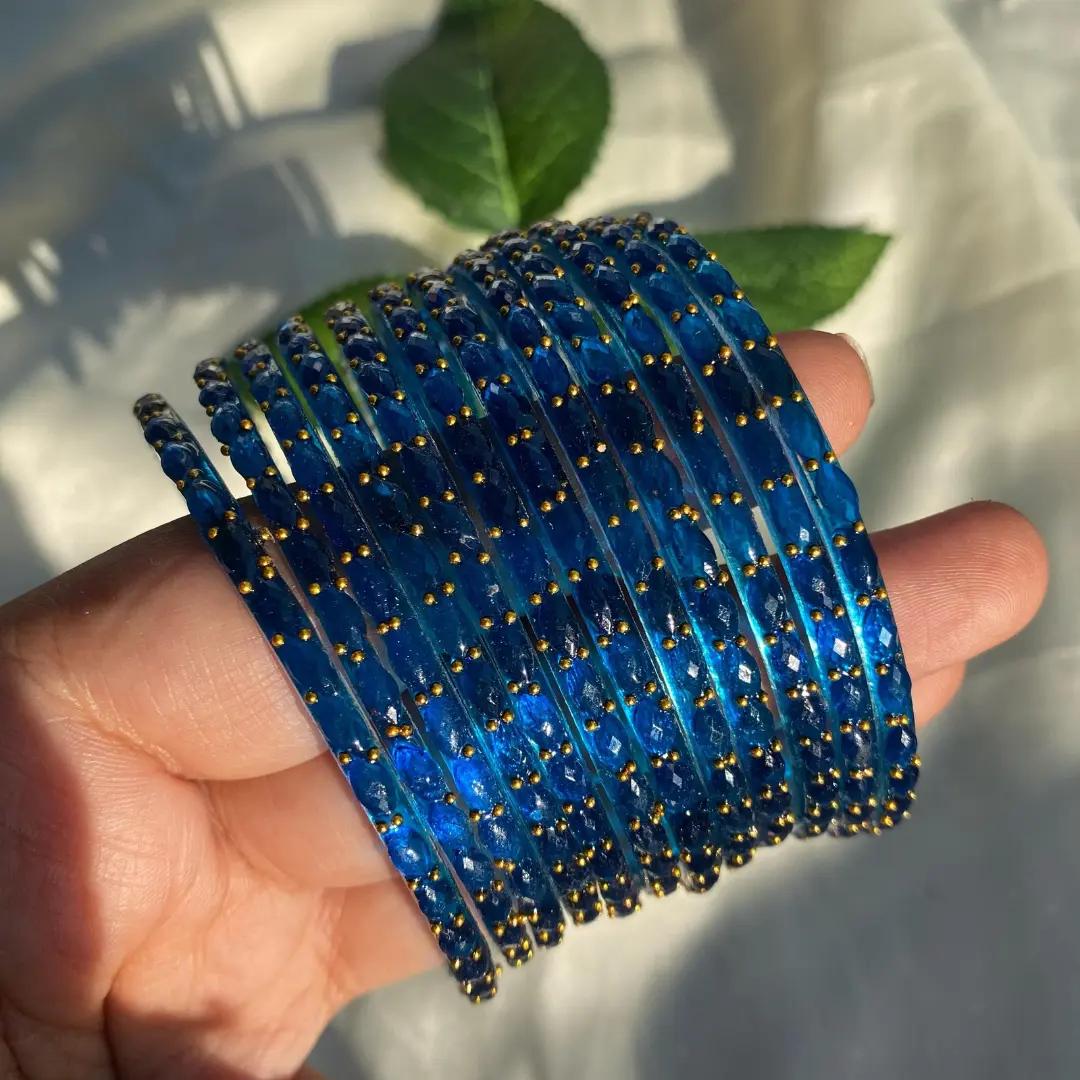 Deep blue faceted glass bangles stacked on a wrist, dotted with small gold beads