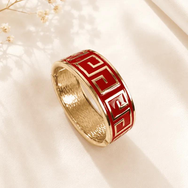 Broad red enamel kada with gold-tone Greek key pattern and textured golden interior standing on satin