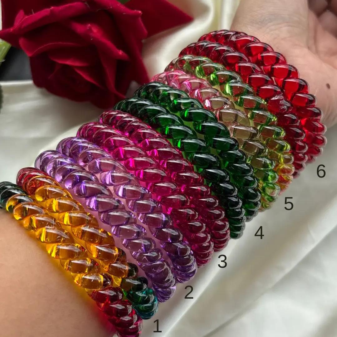 Rope-twist glass bangles in amber, purple, magenta, green and red worn stacked on a wrist, numbered by design