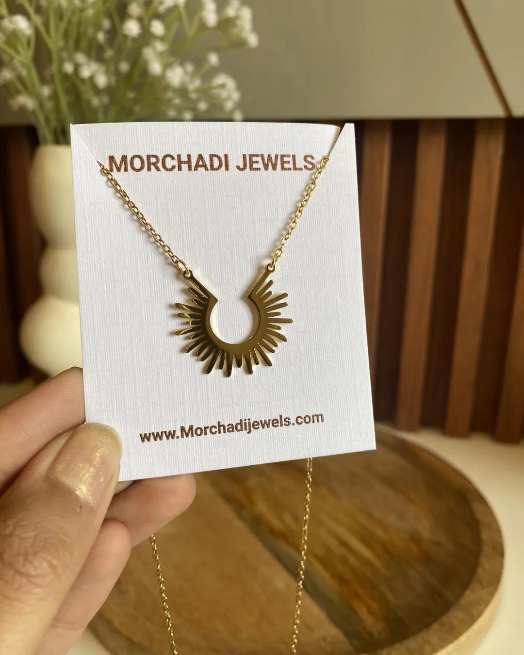 Gold-plated open sunburst pendant with alternating long and short rays on a fine chain, shown on a white card