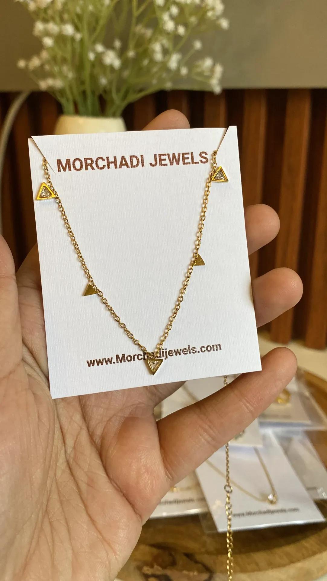 Fine gold-plated necklace with five small triangle charms, some stone-set, displayed on a white brand card