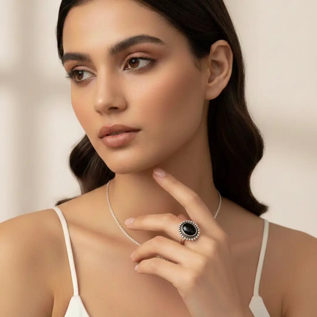Silver-finish ring with a round black stone set in a beaded oval frame, worn on a finger