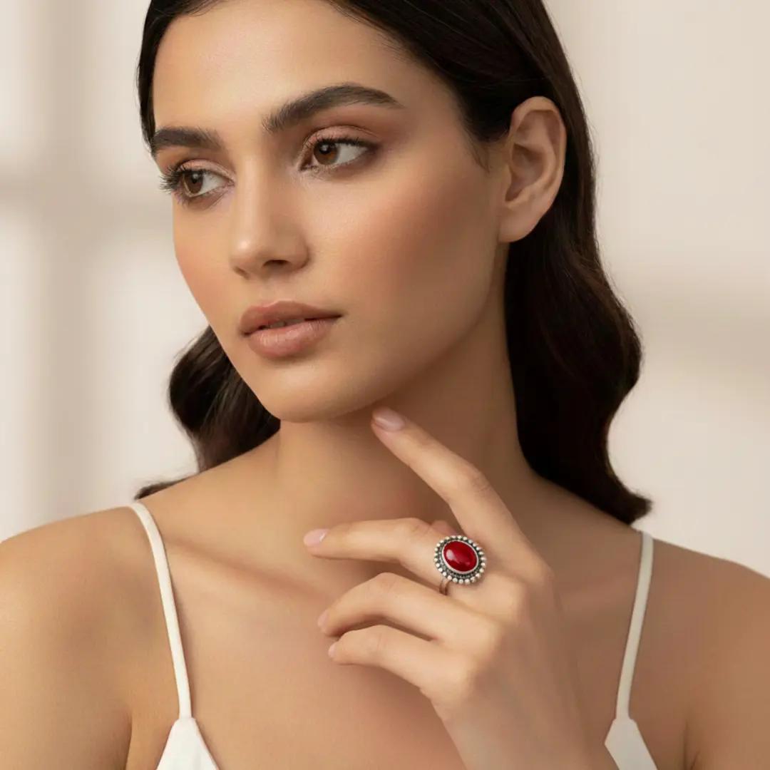 Silver-finish ring with a glossy red oval stone in a beaded frame, worn on a finger