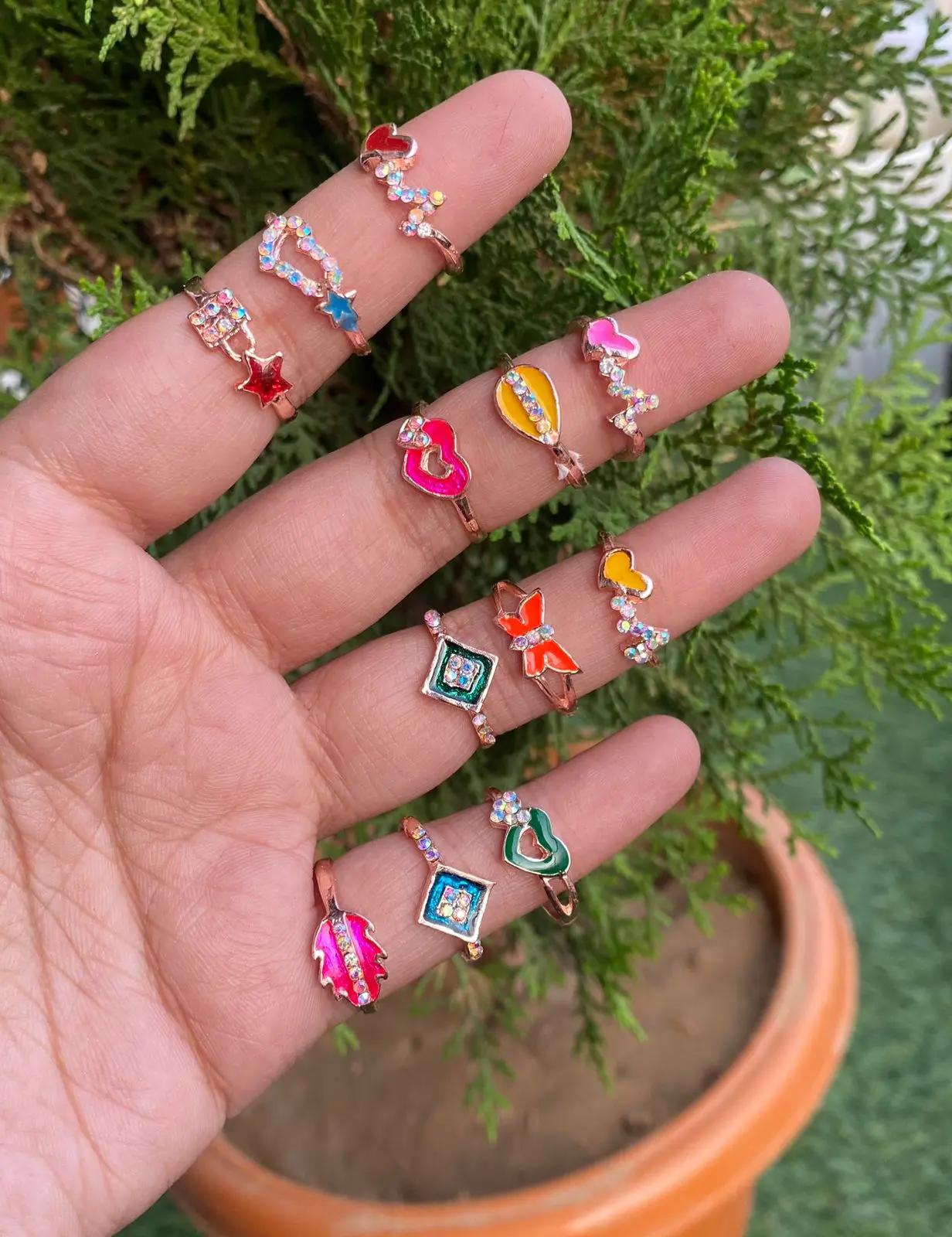 Set of twelve small enamel motif rings in rose gold-plated metal, worn across several fingers