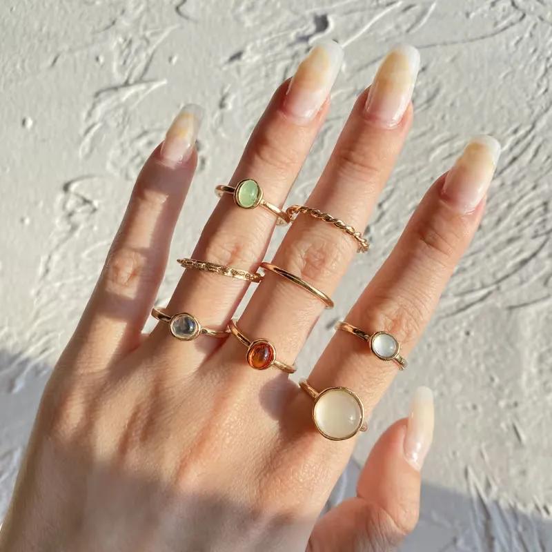 Eight slim gold-colour rings with milky pastel stones worn stacked across the fingers of one hand