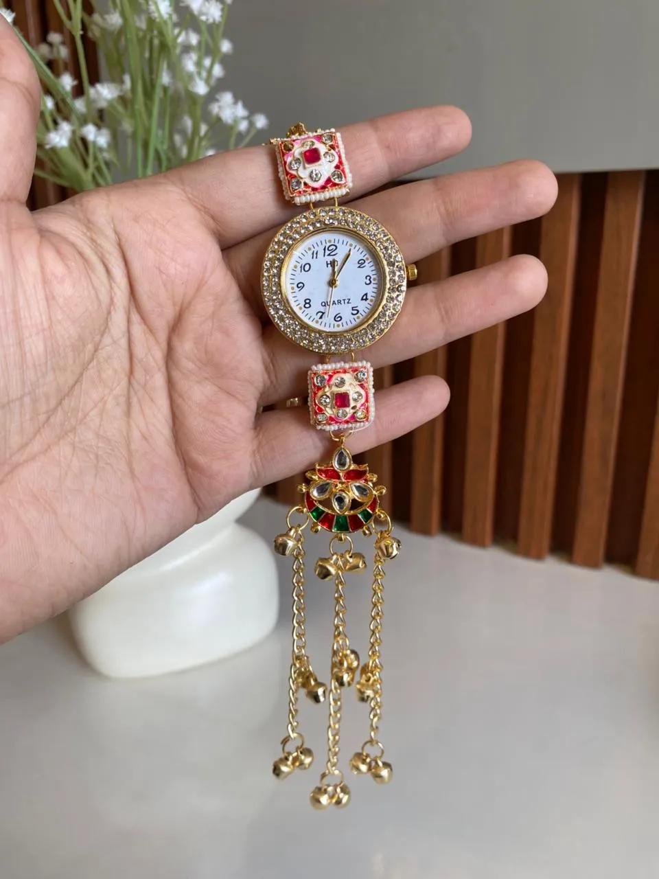 Gold-tone bracelet watch with soft pink meenakari panels and a moon-shaped kundan pendant