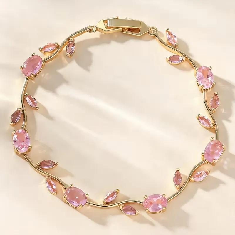 Slim gold-tone vine bracelet set entirely with pale pink oval and marquise stones, coiled on a cream ground