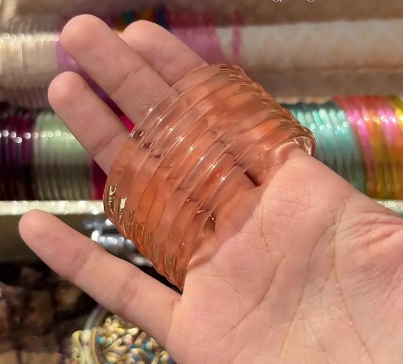 Stack of eight translucent peach glass bangles worn on a wrist