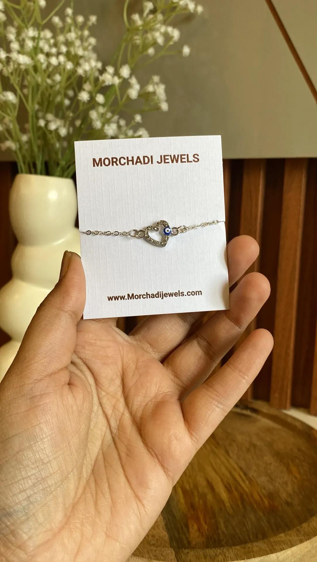 Fine silver-toned bracelet with an open heart outline of small stones and a blue evil eye bead at its top