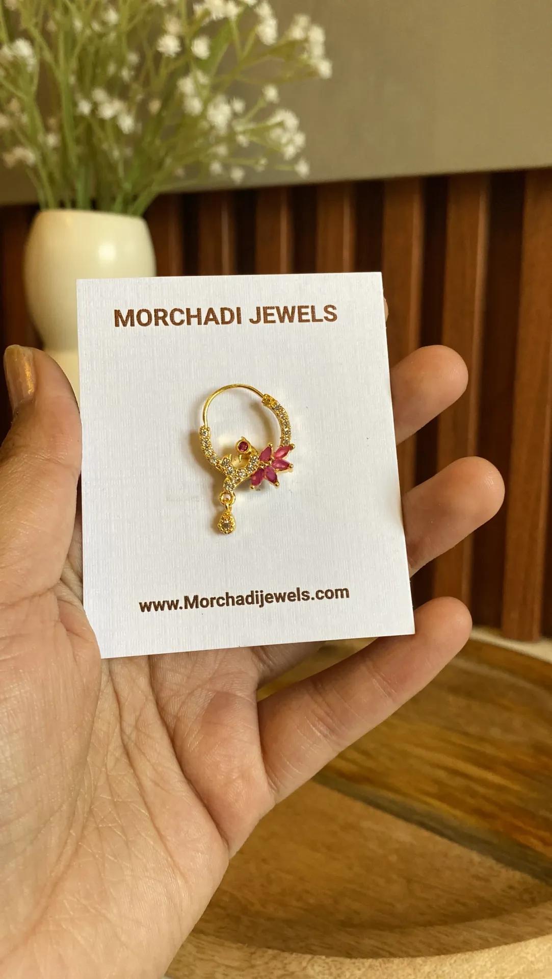Gold-toned nath with white stones along the hoop, a red marquise-petal flower and a small drop, held on a white card