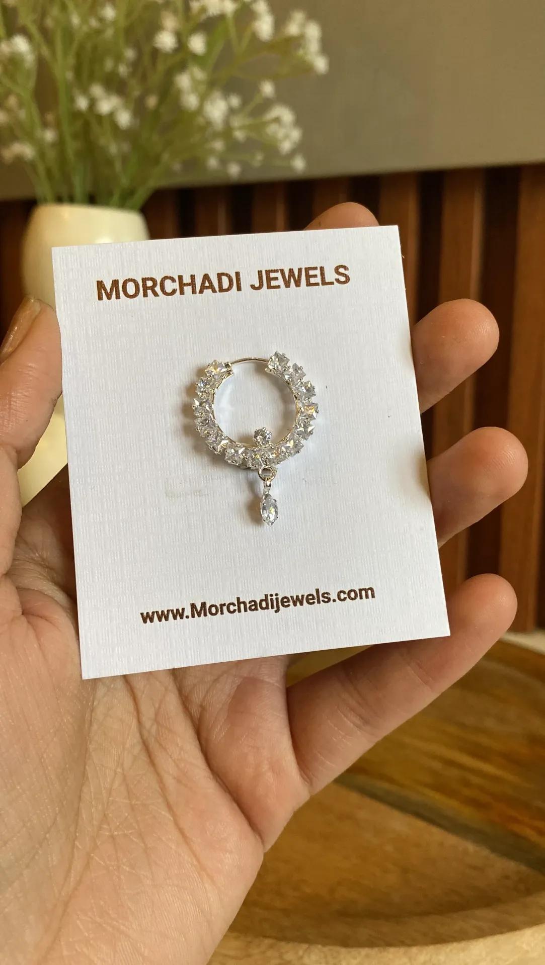 Silver-toned nath with clear cubic zirconia stones set around the ring and a small teardrop drop