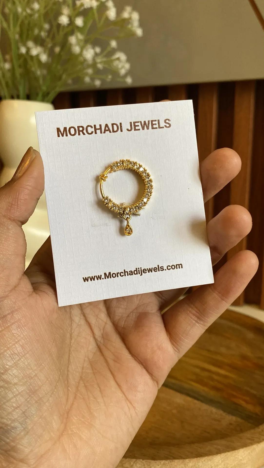 Gold-toned nath with a hook opening, a small dense cluster of clear stones and a teardrop charm