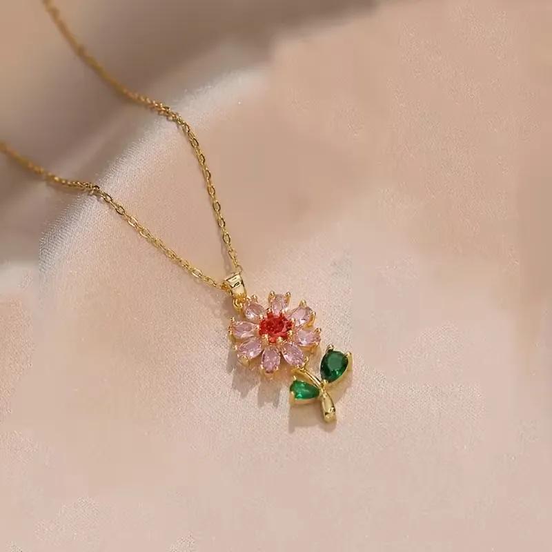 Gold-toned pendant necklace with a pink flower charm, red centre and green leaf accents