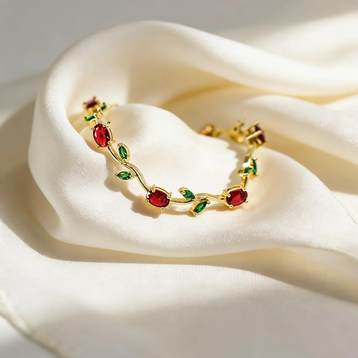Gold-toned chain-link bracelet with red oval stones and green leaf accents along a vine design