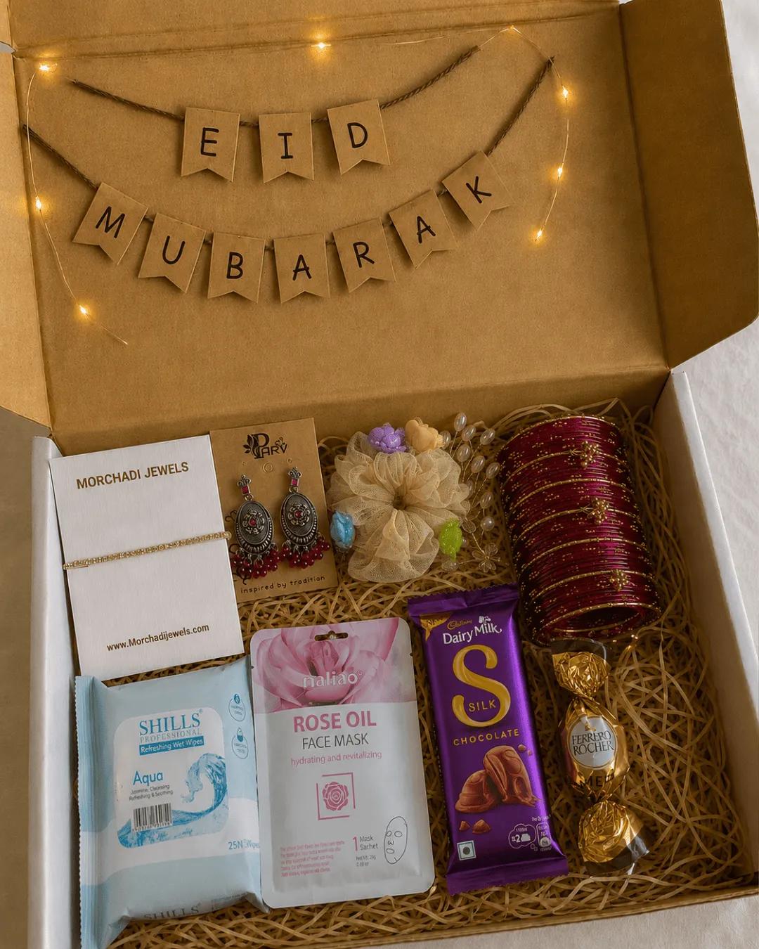 Eid Mubarak gift hamper open to show a bracelet, earrings, maroon bangles, face mask and chocolates