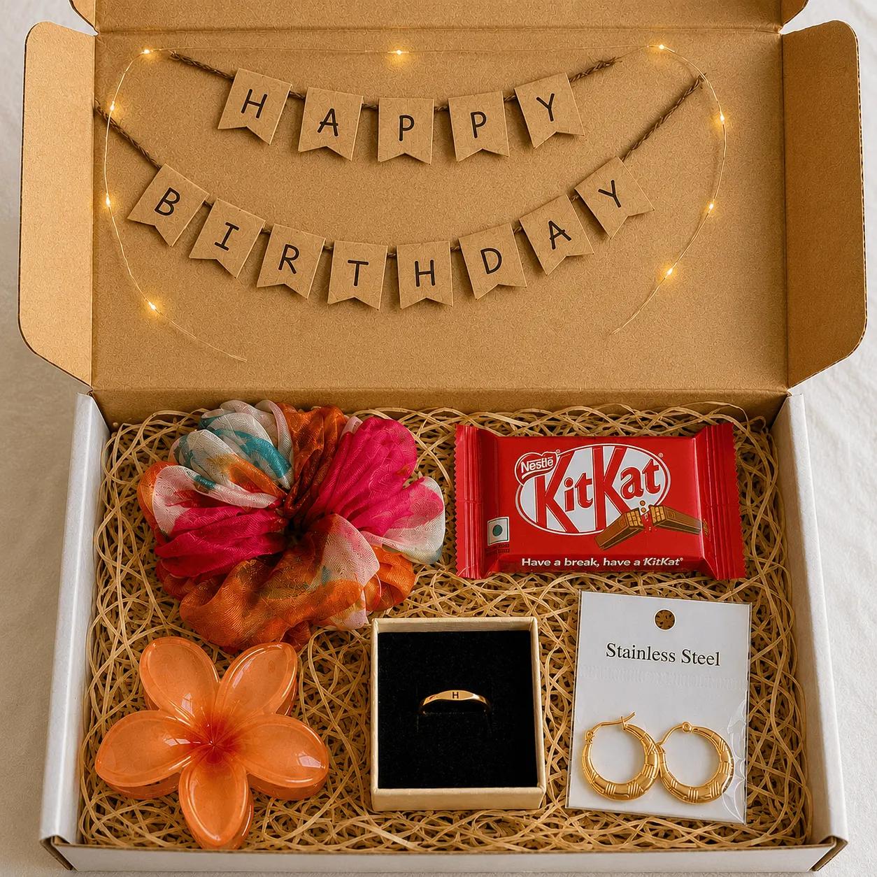 Small birthday hamper with a gold initial ring, hoop earrings, a scrunchie and a flower hair clip