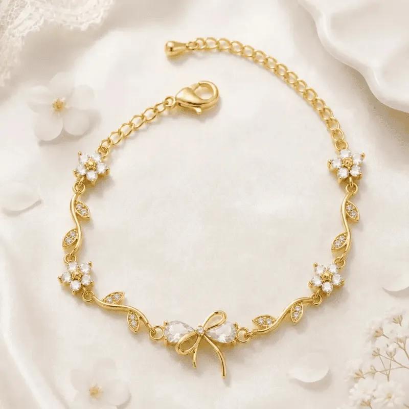 Gold-toned bracelet with clear white faceted stone blossoms, pave leaves and a stone-set bow charm