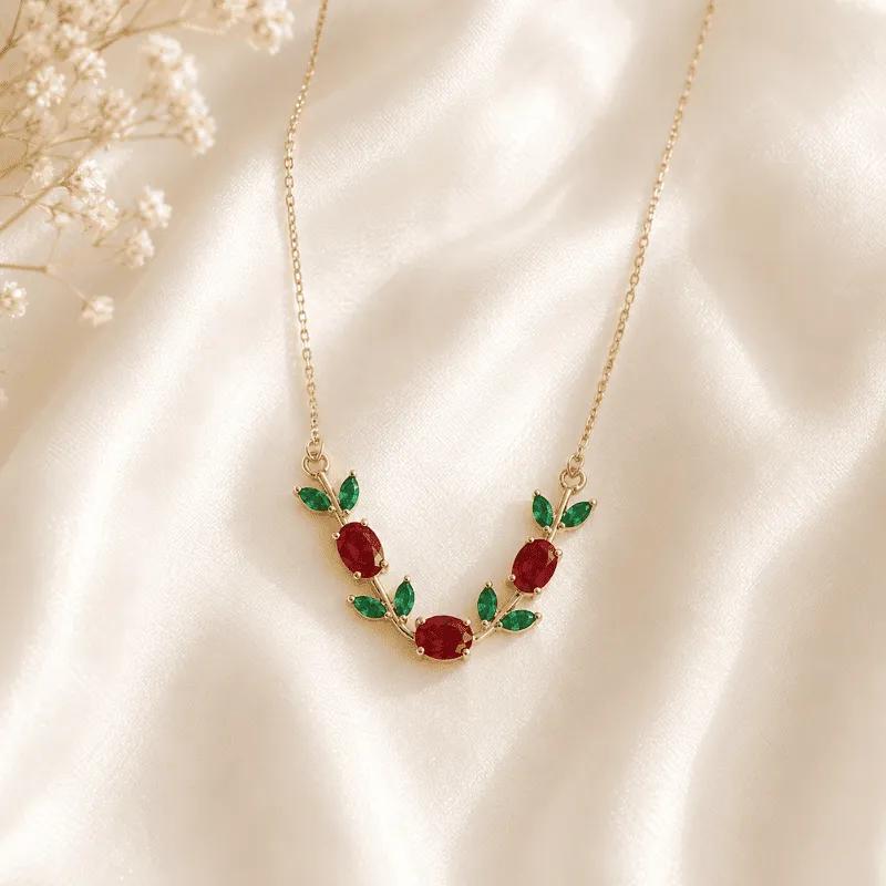 Gold-plated V-shaped vine necklace with red cubic zirconia stones and emerald-green leaf accents