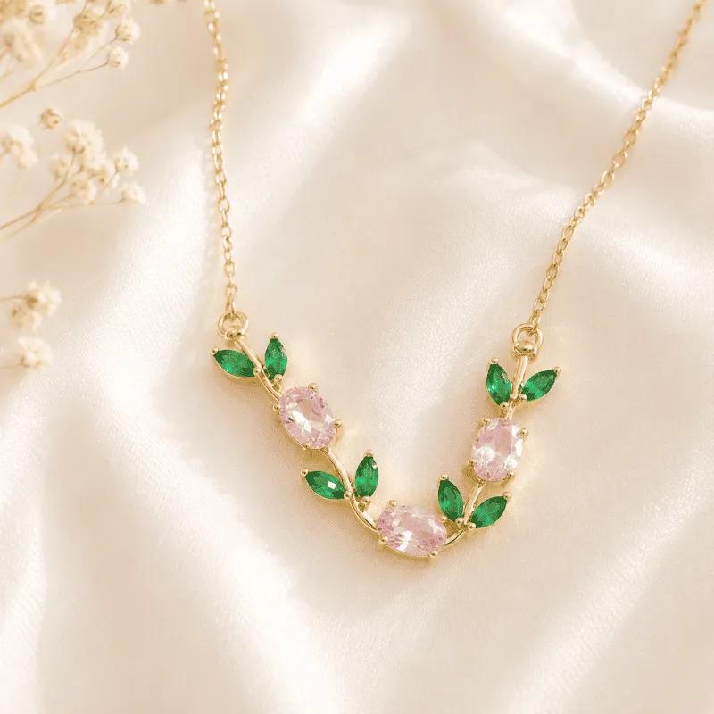 Gold-plated V-shaped vine necklace with blush pink cubic zirconia stones and emerald-green leaf accents