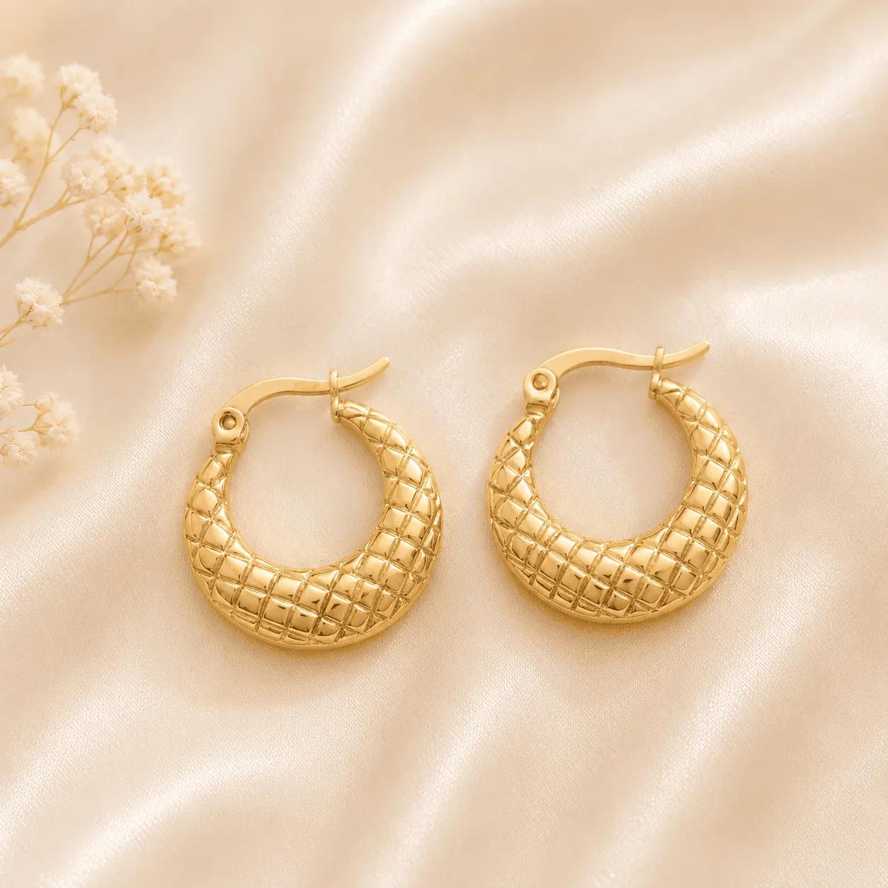 Wide gold-plated steel crescent hoop earrings with a raised quilted diamond-grid texture