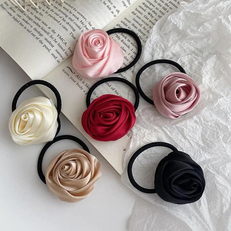 Six satin rose hair ties in pink, cream, red, mauve, champagne and black arranged on an open book