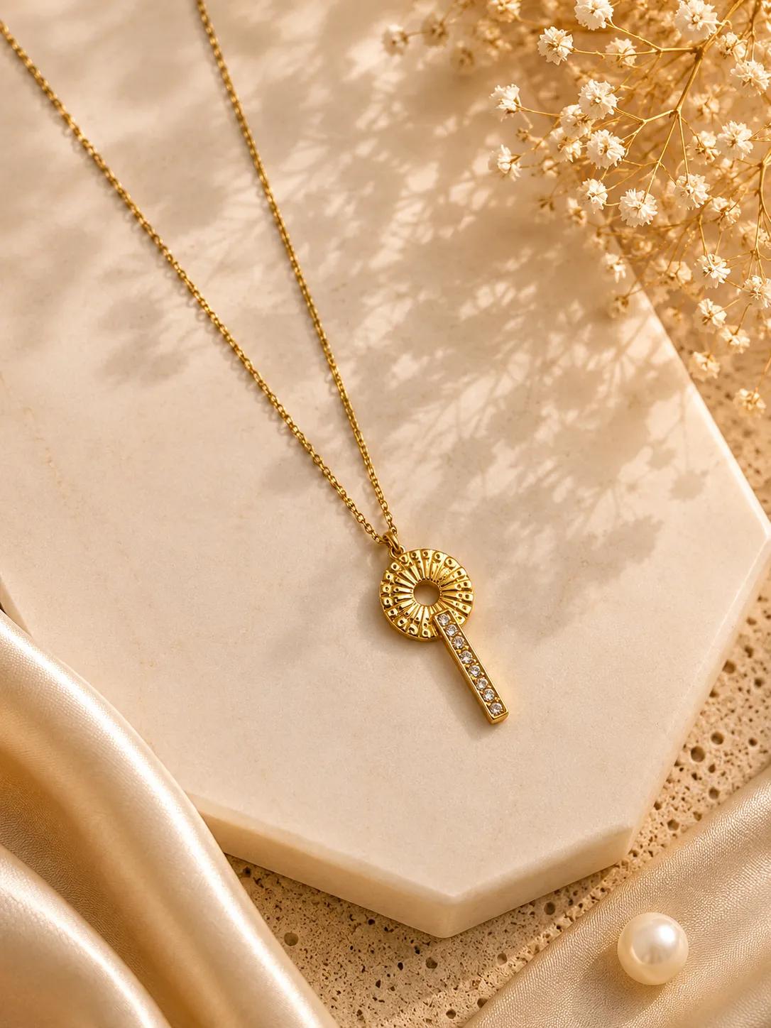 Gold-tone key-shaped pendant with a textured sunburst medallion and clear cubic zirconia bar