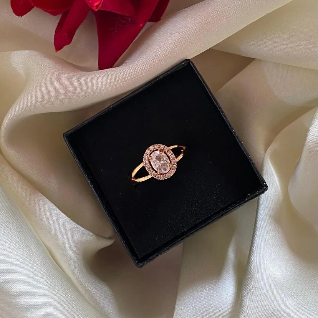 Oval cubic zirconia centre stone with a full pavé halo on a slim rose gold-plated ring, on a black box