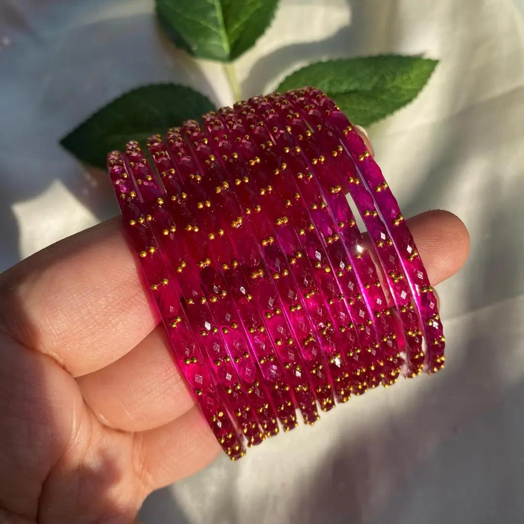 Bright pink faceted glass bangles in a full stack, edged with small gold beads