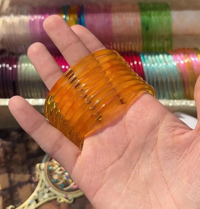 Stack of eight translucent caramel amber glass bangles worn on a wrist